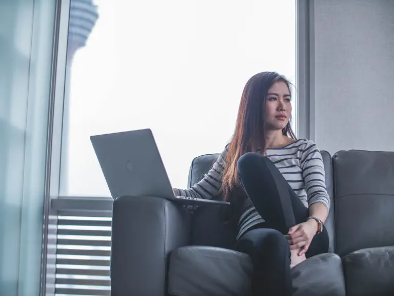 Thoughtful woman sitting on sofa with laptop