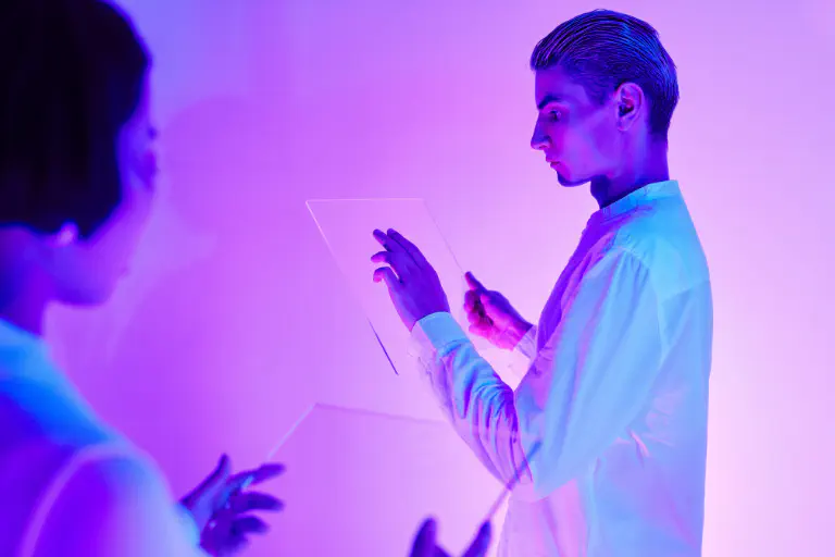 Two people dressed in white hold panes of glass like technical devices in purple light.