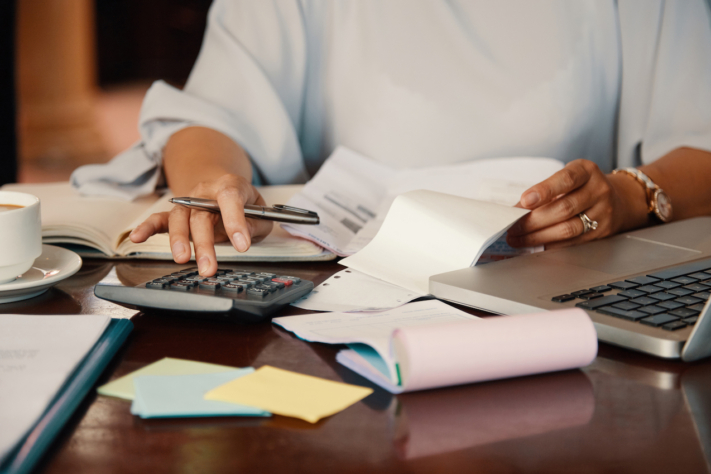 Travel expense report: A woman is doing paperwork and typing into a calculator.