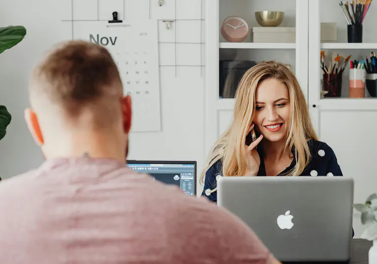 Two employees sit at their laptop and enter their vacation