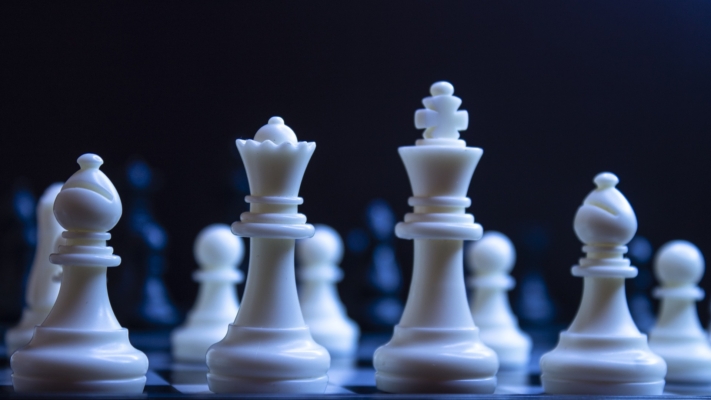 Des pièces d’échecs blanches au premier plan, des pièces d’échecs noires à l’arrière-plan.